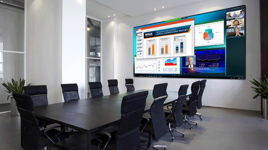 A modern conference room with a large wall-mounted display showing financial charts, video call screens, and business presentation content.